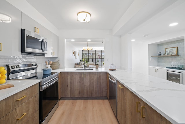 kitchen featuring kitchen peninsula, backsplash, a notable chandelier, light wood-type flooring, and stainless steel appliances