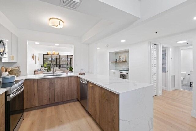 kitchen with light stone countertops, a notable chandelier, sink, light hardwood / wood-style flooring, and stainless steel appliances