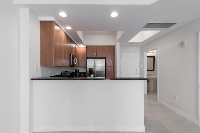 kitchen with a skylight, kitchen peninsula, appliances with stainless steel finishes, and light tile patterned floors