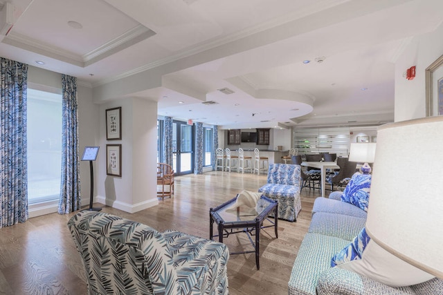 living room with light hardwood / wood-style floors, a raised ceiling, and crown molding