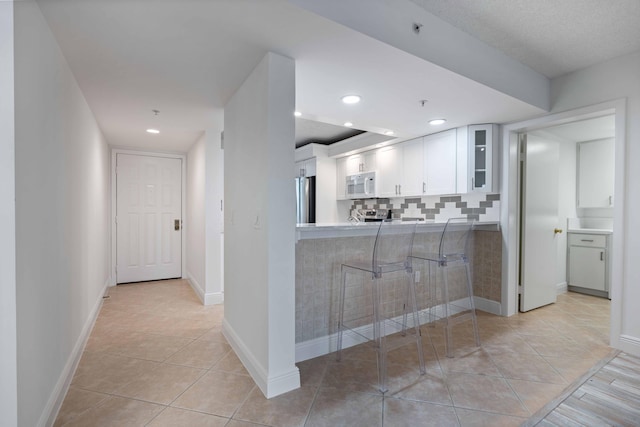 kitchen with stainless steel refrigerator, tasteful backsplash, white cabinets, light tile floors, and kitchen peninsula