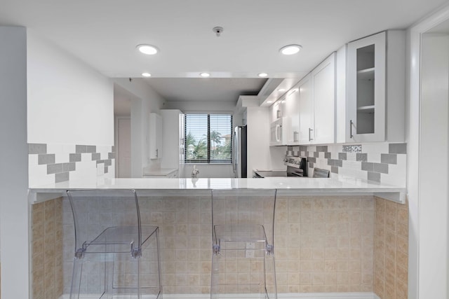 kitchen featuring stainless steel fridge, electric range oven, kitchen peninsula, light stone countertops, and white cabinets