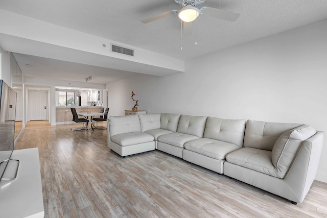 living room featuring light hardwood / wood-style flooring, ceiling fan, and a textured ceiling