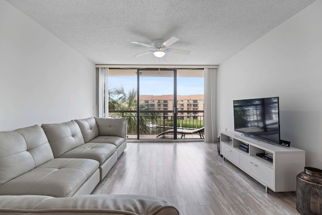 living room featuring ceiling fan, expansive windows, light wood-type flooring, and a textured ceiling