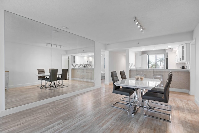 dining space with light hardwood / wood-style flooring, track lighting, and a textured ceiling