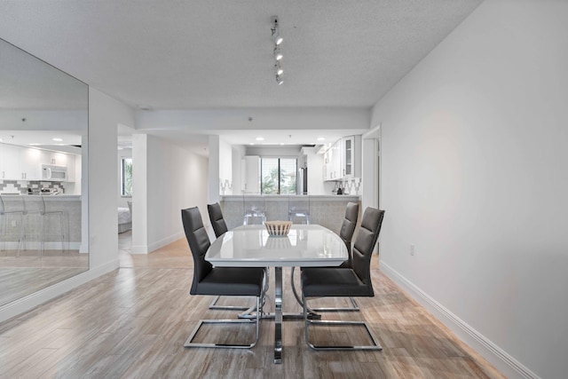 dining room featuring a textured ceiling, light hardwood / wood-style floors, and rail lighting