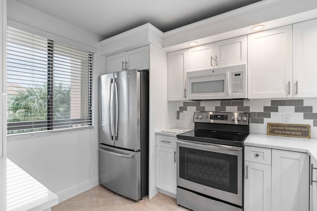 kitchen featuring appliances with stainless steel finishes, white cabinets, light tile floors, and backsplash