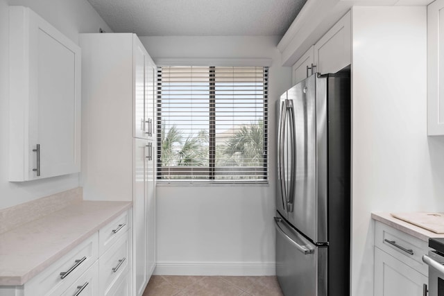 kitchen featuring light tile flooring, stainless steel refrigerator, and white cabinets