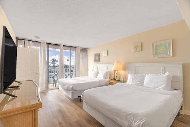 bedroom with a textured ceiling, access to exterior, light wood-style flooring, and expansive windows