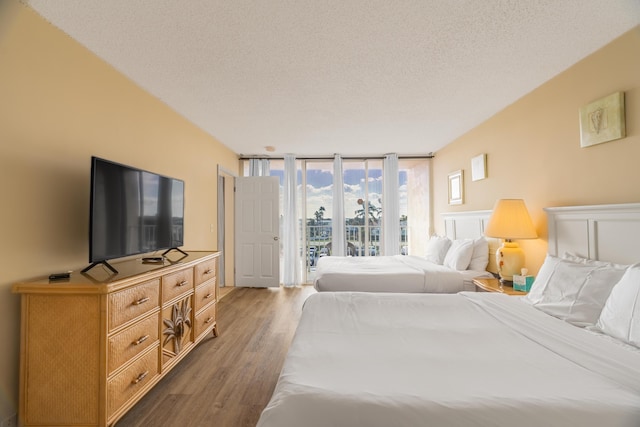 bedroom featuring a wall of windows, wood finished floors, a textured ceiling, and access to exterior