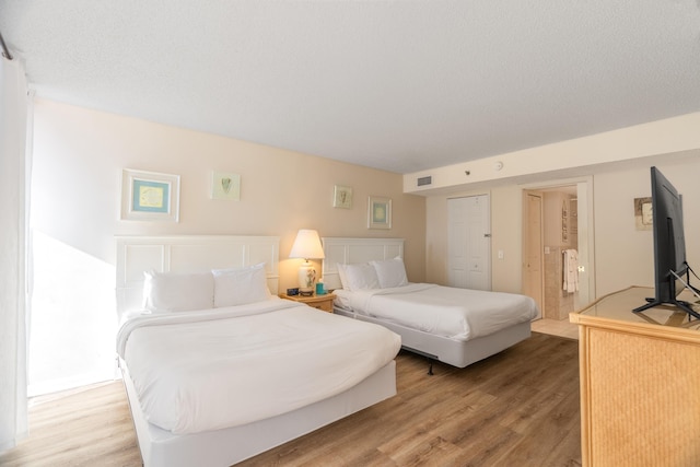 bedroom featuring ensuite bathroom, visible vents, light wood finished floors, and a textured ceiling