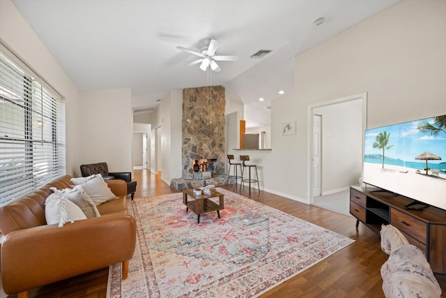 living room with dark hardwood / wood-style floors, ceiling fan, vaulted ceiling, and a stone fireplace