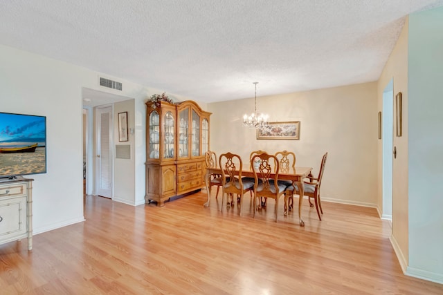 dining area featuring a chandelier, light hardwood / wood-style floors, and a textured ceiling