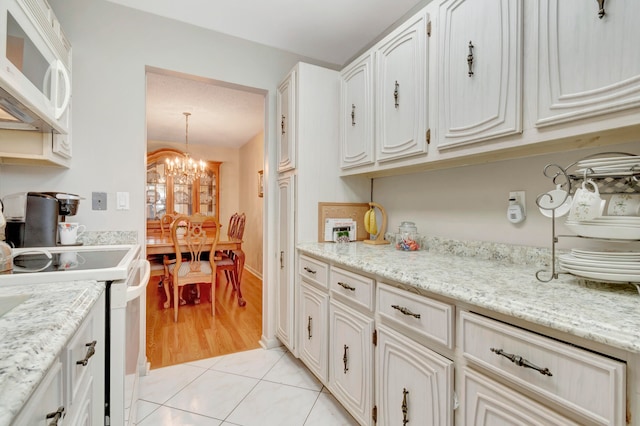 kitchen with a chandelier, light tile flooring, white appliances, white cabinetry, and light stone counters