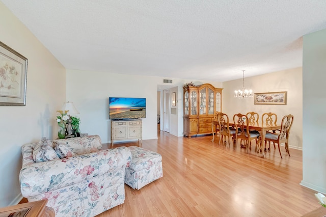 living room featuring an inviting chandelier, light hardwood / wood-style floors, and a textured ceiling