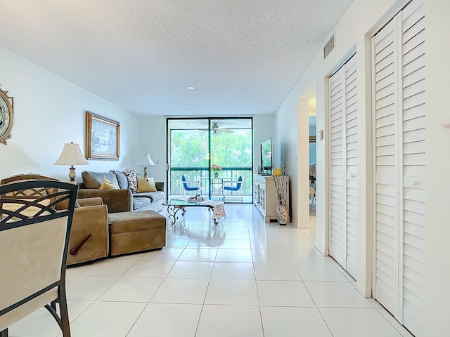 living room featuring light tile flooring, a wall of windows, and a textured ceiling