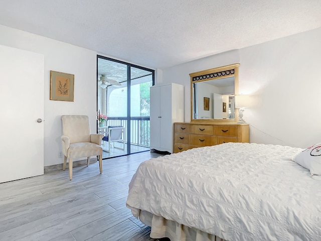 bedroom featuring expansive windows, access to exterior, light hardwood / wood-style flooring, and a textured ceiling