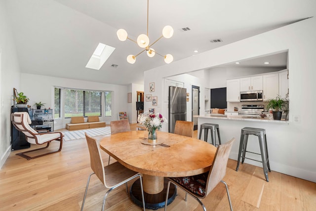 dining space featuring vaulted ceiling with skylight, light wood-type flooring, and an inviting chandelier