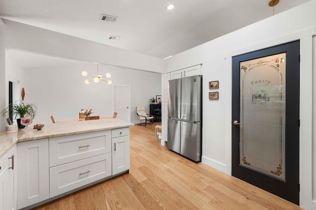 kitchen featuring stainless steel refrigerator, white cabinetry, decorative light fixtures, and light wood-type flooring