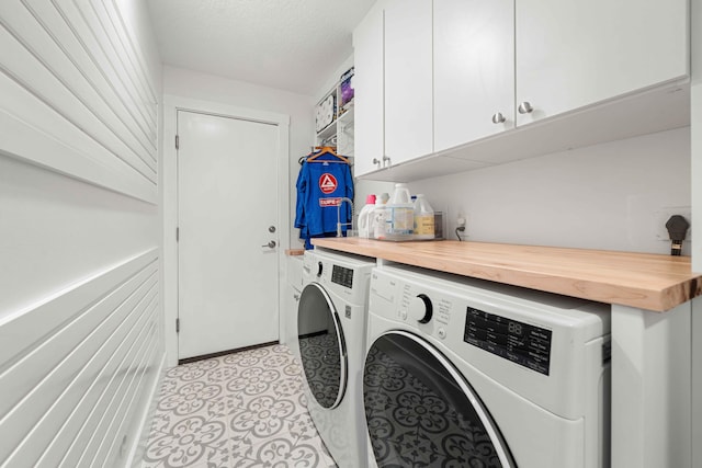 clothes washing area with cabinets, a textured ceiling, and washer and clothes dryer