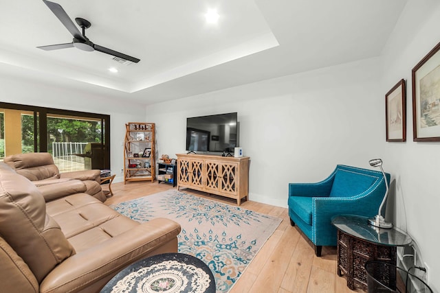 living room with ceiling fan, a tray ceiling, and light hardwood / wood-style flooring