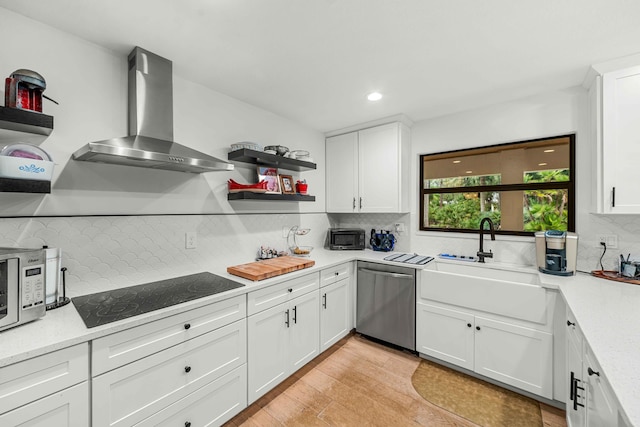 kitchen featuring black electric stovetop, white cabinets, wall chimney exhaust hood, light hardwood / wood-style flooring, and dishwasher