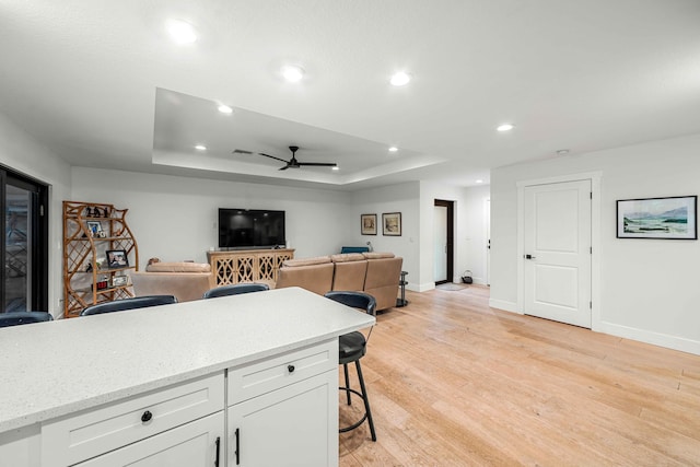 kitchen featuring light wood-type flooring, a breakfast bar, a raised ceiling, ceiling fan, and white cabinets