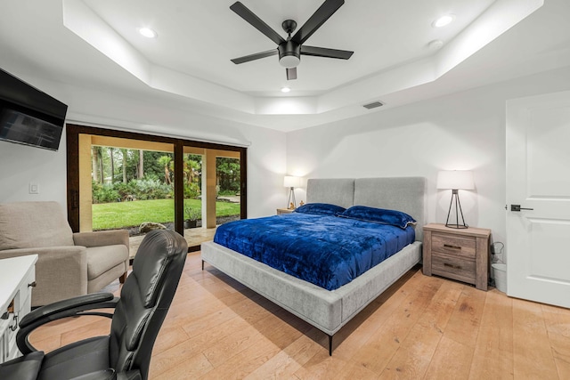 bedroom with ceiling fan, light hardwood / wood-style floors, and a tray ceiling