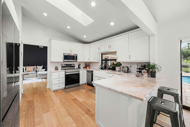 kitchen featuring white cabinetry, kitchen peninsula, appliances with stainless steel finishes, and a skylight