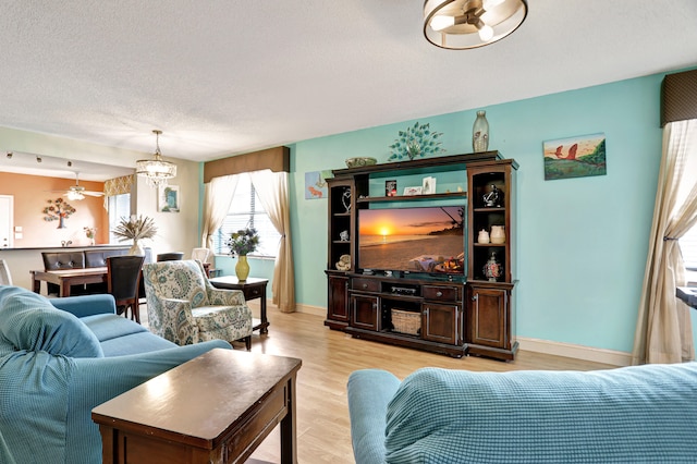 living room featuring ceiling fan with notable chandelier, a textured ceiling, and light wood-type flooring