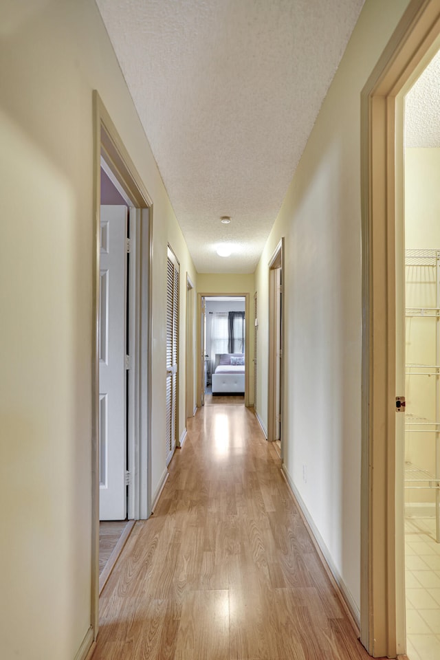 hall with a textured ceiling and light hardwood / wood-style floors