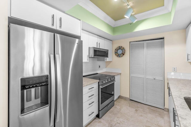 kitchen featuring white cabinets, decorative backsplash, light stone countertops, appliances with stainless steel finishes, and a tray ceiling