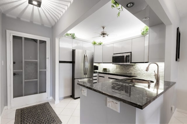 kitchen with kitchen peninsula, tasteful backsplash, appliances with stainless steel finishes, white cabinets, and sink