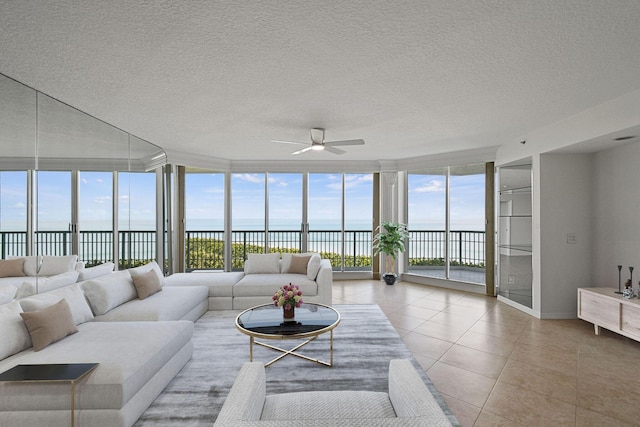 living area with a water view, ceiling fan, a textured ceiling, a wall of windows, and tile patterned flooring