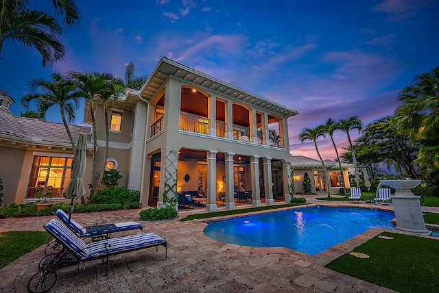 pool at dusk with a patio and pool water feature