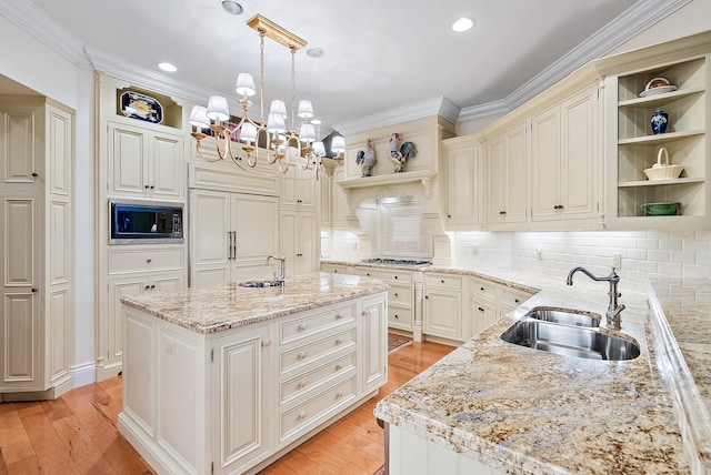 kitchen featuring a chandelier, built in appliances, decorative light fixtures, a kitchen island with sink, and sink