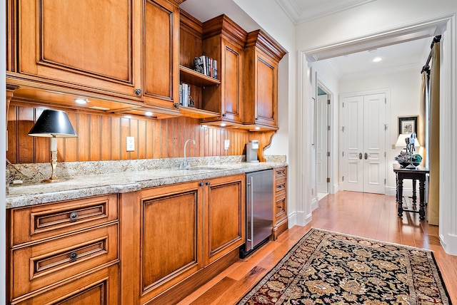 kitchen with light stone counters, crown molding, light hardwood / wood-style floors, and sink