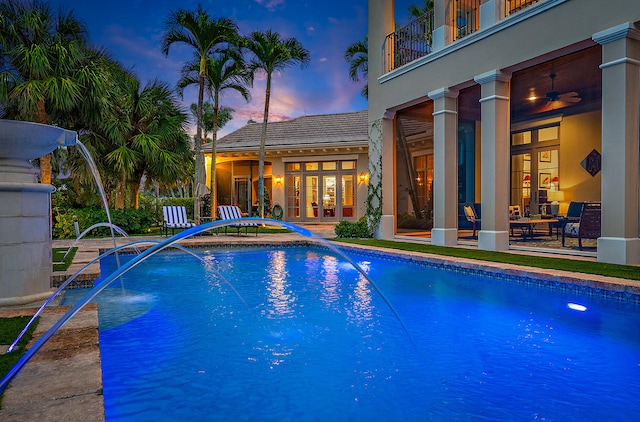 pool at dusk with a patio area, pool water feature, and french doors