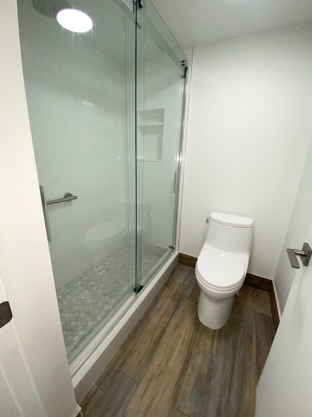 bathroom featuring toilet, a shower with door, and hardwood / wood-style flooring