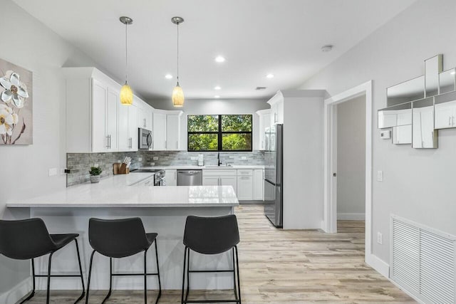 kitchen featuring hanging light fixtures, light hardwood / wood-style flooring, kitchen peninsula, white cabinets, and appliances with stainless steel finishes