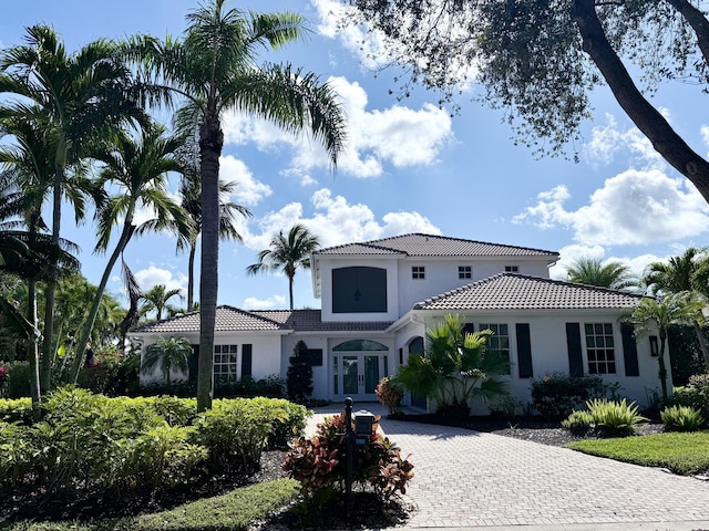 mediterranean / spanish house with a tiled roof, stucco siding, french doors, and driveway