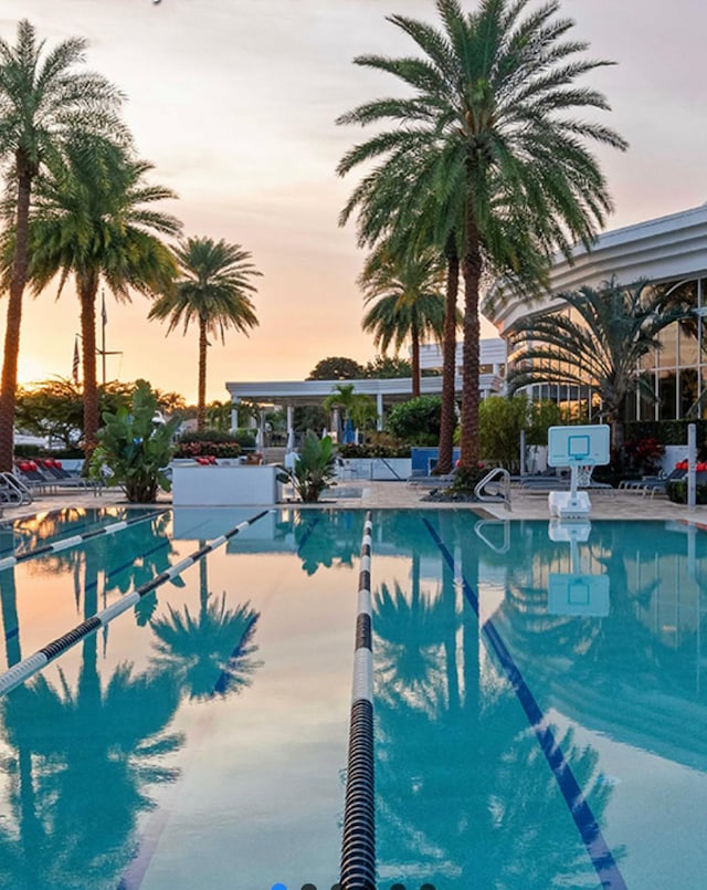 pool at dusk with a patio area and a community pool