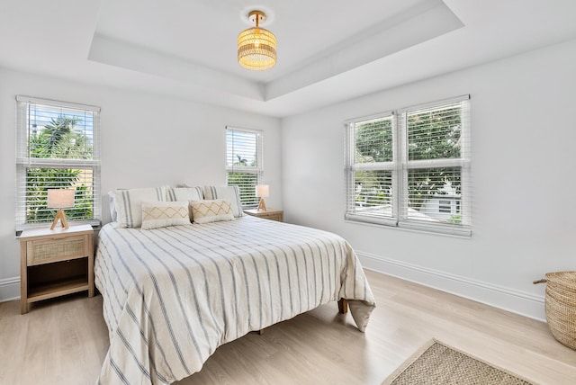 bedroom featuring a raised ceiling, multiple windows, and light hardwood / wood-style floors