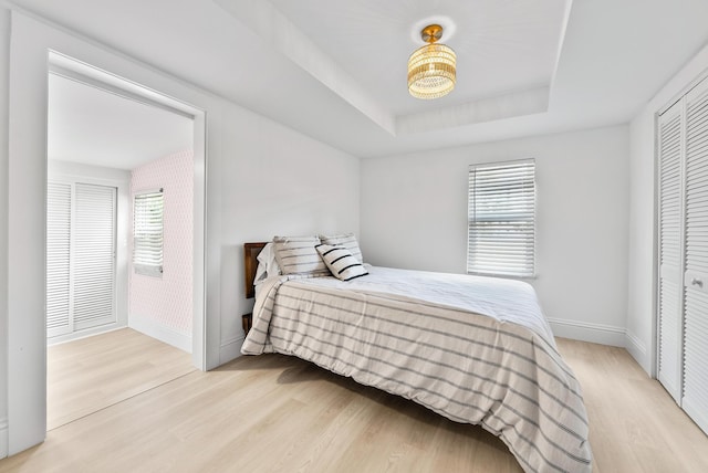 bedroom featuring a closet, a tray ceiling, light hardwood / wood-style floors, and multiple windows