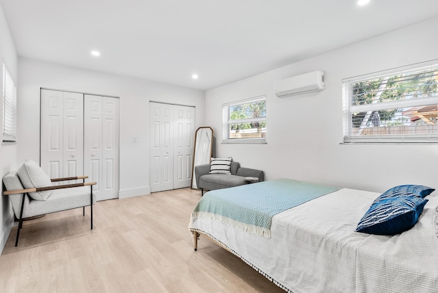 bedroom featuring light hardwood / wood-style floors, an AC wall unit, and multiple closets