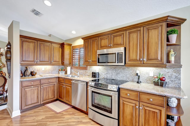 kitchen featuring lofted ceiling, light wood-type flooring, stainless steel appliances, light stone counters, and tasteful backsplash