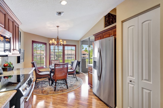 kitchen featuring light stone counters, appliances with stainless steel finishes, light hardwood / wood-style floors, a notable chandelier, and lofted ceiling