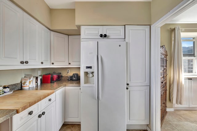 kitchen with light tile patterned floors, white fridge with ice dispenser, light countertops, and white cabinetry