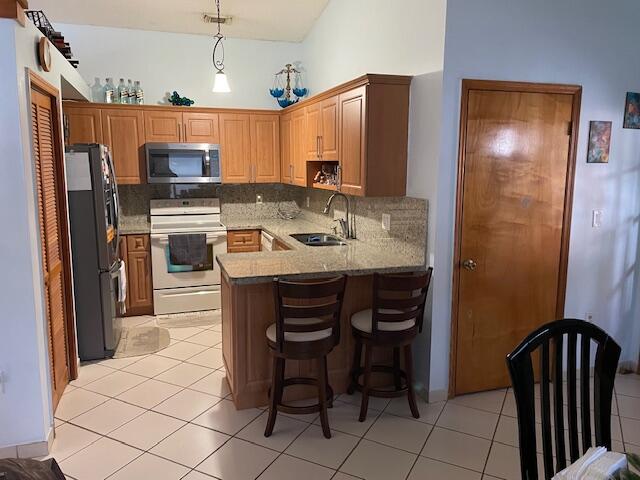 kitchen featuring kitchen peninsula, decorative light fixtures, appliances with stainless steel finishes, sink, and light tile floors