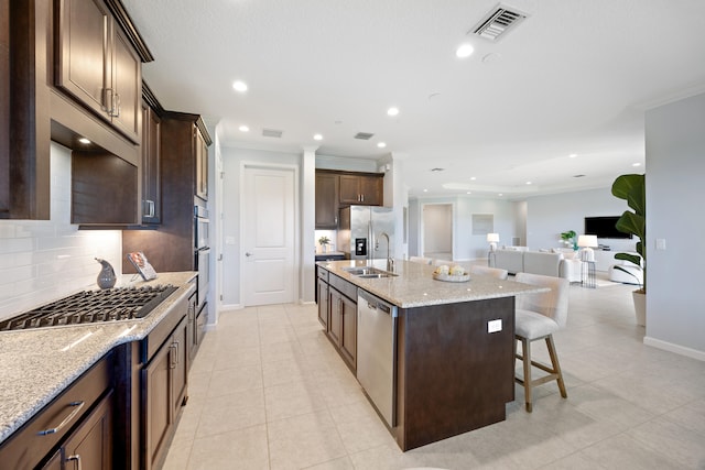 kitchen with a center island with sink, sink, decorative backsplash, appliances with stainless steel finishes, and a kitchen bar